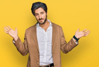 İş kıyafetleri giymiş, elleri ve kolları havada, kafası karışmış genç İspanyol bir adam. şüphe kavramı. 