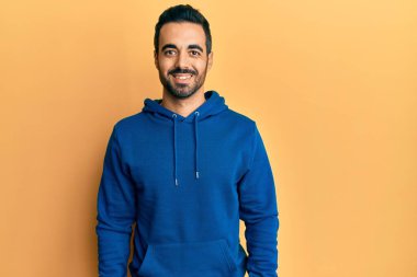 Yüzünde mutlu ve havalı bir gülümseme olan sıradan kıyafetler giyen genç İspanyol bir adam. şanslı kişi. 