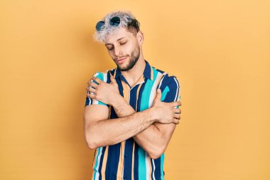 Modern boyalı saçlı, yaz gömleği ve güneş gözlüğü takan mutlu, pozitif ve kendinden emin gülümseyen İspanyol bir genç. Sevgi ve özgüven. 