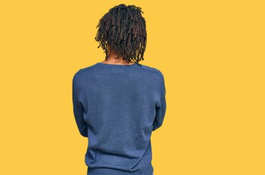 Sıradan bir kazak giyen Afro-Amerikan genç adam arkasını dönüp kollarını kavuşturmuş bakıyor. 