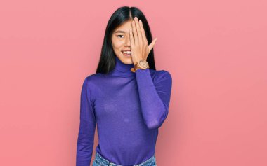 Güzel, genç Asyalı bir kadın gündelik kıyafetler giyip bir gözünü eliyle kapatıyor, yüzünde kendine güvenen bir gülümseme ve sürpriz bir duygu var.. 