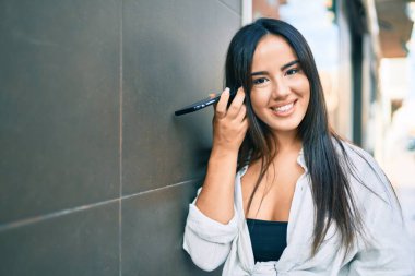 Genç İspanyol kız gülümsüyor. Şehirdeki akıllı telefonu kullanarak mutlu bir sesli mesaj dinliyor..