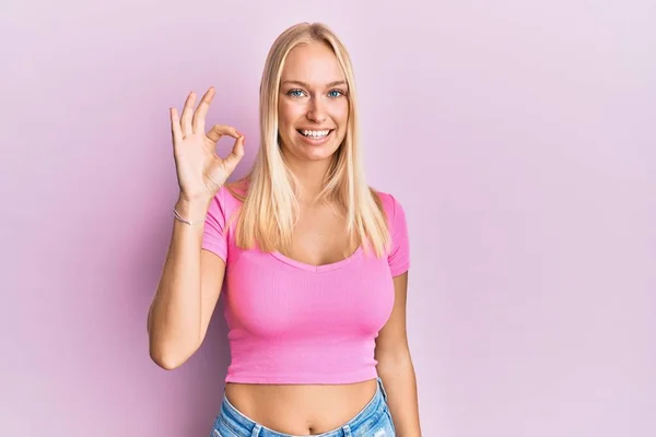 Młoda Blondynka Luźnych Ubraniach Uśmiecha Się Pozytywnie Robi Znak Dłoni — Zdjęcie stockowe