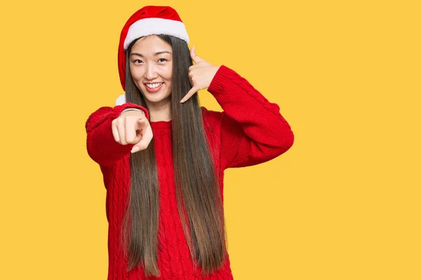 若い中国人女性はクリスマスの帽子を身に着けている笑顔は電話のジェスチャーで話をし あなたを指している 電話してくれ — ストック写真