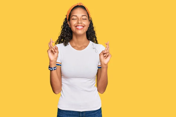 身穿休闲装的年轻的非洲裔美国女孩 用手指做手势 微笑着与希望交手 闭上眼睛 幸运与迷信的概念 — 图库照片