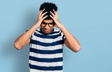 Genç Afro-Amerikan adam gündelik kıyafetler ve gözlük takıyor. Baş ağrısı çekiyor, çaresiz ve stresli. Çünkü acı ve migren. Eller başının üstünde.. 