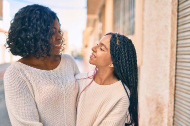 Güzel Afro-Amerikan anne ve kızı gülümsüyor ve sarılıyorlar. Yüzünde tebessümle şehirde dikilirken.