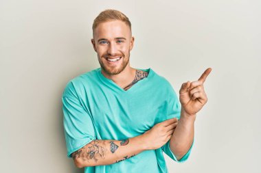 Yüzünde büyük bir gülümseme olan, el ve parmak ile kameraya bakan, günlük kıyafetler giyen genç beyaz bir adam.. 