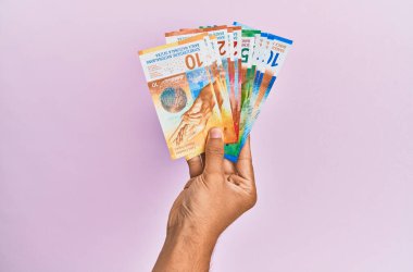 İspanyol eli İsviçre frangı banknotlarını soyutlanmış pembe arka planda tutuyor.