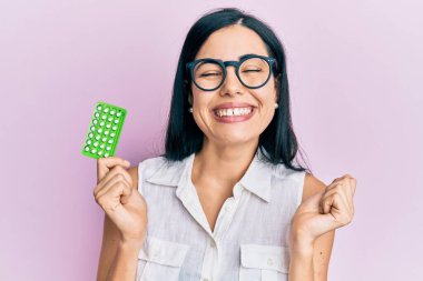 Doğum kontrol hapları tutan güzel genç bir kadın gururla bağırıyor, zaferi kutluyor ve başarıyı kollarını kaldırarak kutluyor. 