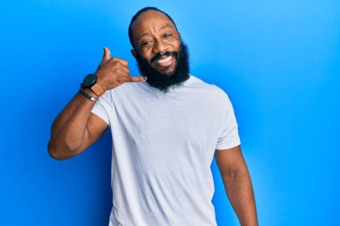 Genç Afro-Amerikalı adam, günlük beyaz tişörtler giyip gülümsüyor telefonla el ve parmaklarıyla jest yapıyor telefonda konuşuyor gibi. iletişim kavramları. 