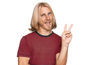 Sarı uzun saçlı, sıradan çizgili tişört giyen, kameraya gülümseyen ve zafer işareti yapan beyaz bir adam. İki numara.. 