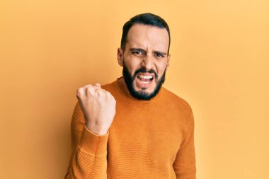 Sakallı genç adam öfkeyle bağırırken kızgın ve kızgın yumruk kaldırıyor. öfke ve agresif konsept. 