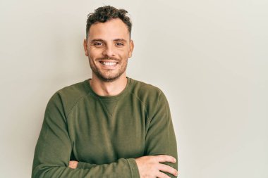 Gündelik kıyafetler giyen, kollarını kavuşturup kameraya gülümseyen genç İspanyol adam. pozitif kişi. 