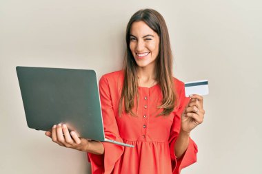 Genç, güzel bir kadın dizüstü bilgisayar ve kredi kartı tutuyor. Kameraya seksi bir ifadeyle bakıyor. Neşeli ve mutlu bir yüzü var.. 