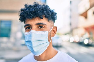 Tıbbi maske takan genç bir Arap şehrin sokağına bakıyor..