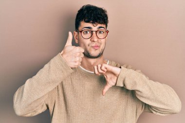 Gündelik kıyafetler giyen ve gözlük takan genç İspanyol bir adam başparmak kaldırıyor, anlaşmazlık ve anlaşma ifadesi. çılgın çatışma 