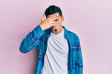 Yakışıklı İspanyol bir adam, günlük giysiler giymiş. Şoka girmiş, yüzünü ve gözlerini kapamış, utanmış bir ifadeyle parmaklarından bakıyor.. 