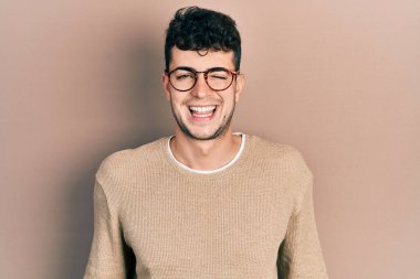 Gündelik kıyafetler giyen ve gözlüklü genç İspanyol adam kameraya seksi bir ifadeyle bakıyor, neşeli ve mutlu bir yüzle.. 