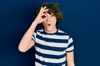 Normal çizgili tişört giyen yakışıklı genç adam şaşırmış yüz ifadesiyle şaşırmış, parmaklarından içeri bakıyor. İnançsız ifade. 