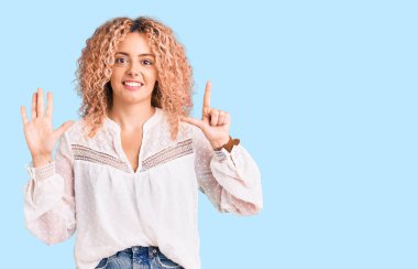 Kıvırcık saçlı, zarif yaz gömleği giyen genç sarışın kadın yedi numaralı parmaklarını gösterip işaret ederken kendine güvenen ve mutlu bir şekilde gülümsüyor.. 