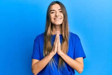 Gündelik giysiler giyen genç İspanyol kadın elleriyle dua ediyor af diliyor kendinden emin bir şekilde gülümseyerek.. 