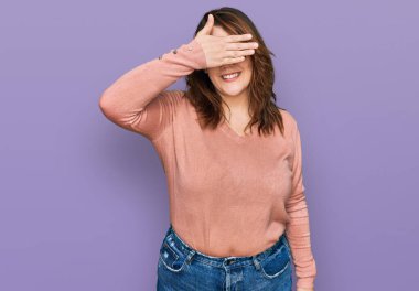 Gündelik kıyafetler ve gözlük takan genç ve cüsseli bir kadın. Gülümsüyor ve elleri yüzünde, şaşkınlıktan gözleri kapatıyordu. kör kavram. 