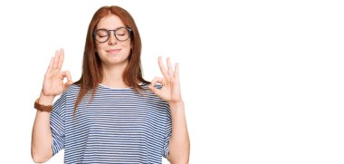 Gündelik kıyafetler ve gözlük takan, gözleri kapalı gülümseyen, meditasyon yapan, parmaklarıyla hareket eden genç, okumuş bir kadın. yoga konsepti. 