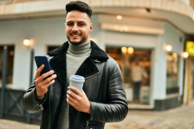 Genç Arap adam akıllı telefon kullanıyor ve şehirde kahve içiyor..