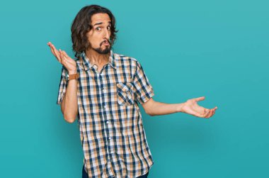 Sıradan kıyafetler giyen, elleri ve kolları havada, kafası karışmış genç İspanyol bir adam. şüphe kavramı. 