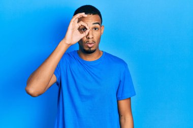 Sıradan mavi tişört giyen genç Afro-Amerikalı adam şaşırmış yüz ifadesiyle şaşırmış ve parmaklarından içeri bakıyor. İnançsız ifade. 