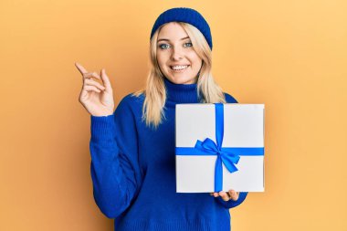 Genç beyaz kadın, elinde hediyeyle mutlu bir şekilde gülümsüyor. 