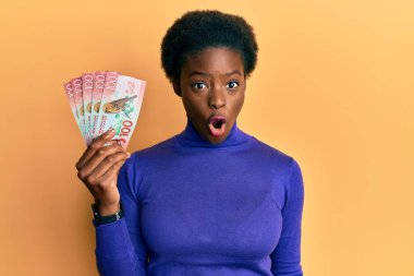 Genç Afrikalı Amerikalı kız elinde 100 yeni Zelanda doları tutuyor. Banknot korkmuş ve şaşırmış bir şekilde ağzı açık kalmış, inançsız bir yüz. 