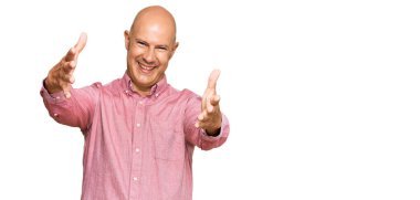 Orta yaşlı kel bir adam, sıradan kıyafetler giyip kameraya bakıyor ve sarılmak için kollarını açmış gülümsüyor. Mutluluğu kucaklayan neşeli bir ifade.. 