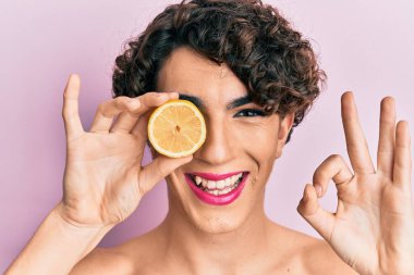 Limon tutan genç adam makyajını yapıyor. Parmaklarıyla imza atıyor. Gülümsüyor. 