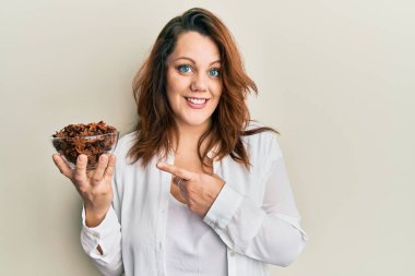 Beyaz bir kadın elinde bir kase yıldız anason tutarken mutlu bir şekilde el ve parmağıyla işaret ediyor. 