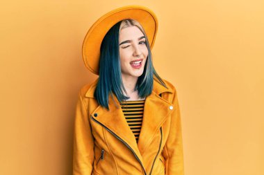 Sarı şapkalı ve deri ceketli genç modern kız kameraya seksi bir ifadeyle bakıyor, neşeli ve mutlu bir yüzle.. 