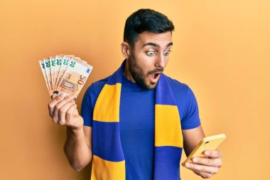 Genç İspanyol futbolcu destekçisi elinde 50 avroluk banknotla korku ve şaşkınlık ifadesi, korku ve heyecanlı yüz ifadesiyle şok oldu.. 