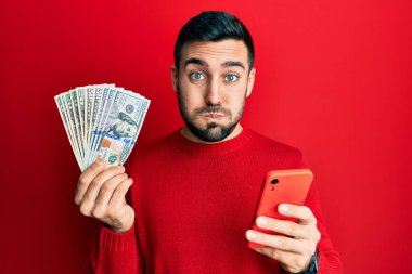 Genç İspanyol adam akıllı telefon kullanıyor ve elinde dolarlarla komik suratını şişiriyor. Ağzı havayla şişer, havayı yakalar.. 