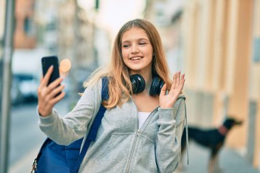 Güzel beyaz öğrenci gülümseyerek şehirde akıllı telefon kullanarak video araması yapıyor..