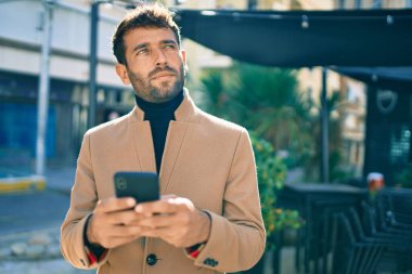Zarif ceketli yakışıklı bir iş adamı. Açık havada akıllı telefon kullanıyor.