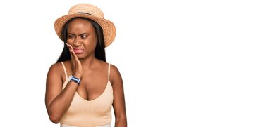 Yazlık şapkalı genç bir kadın diş ağrısı ya da diş hastalığından dolayı ağızlarına acı dolu bir ifadeyle dokunuyor. dişçi 