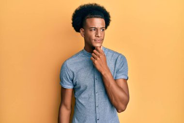 Afro saçlı Afro-Amerikan bir adam günlük giysiler giyiyor şüpheye odaklanmış, çenesinde parmak olan ve kafasını kaldırıp merak eden biri. 