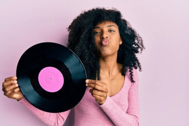 Afro saçlı Afro-Amerikalı bir kadın elinde vinil diskle komik suratlı yanakları şişiriyor. Ağzı havayla şişer, havayı yakalar.. 
