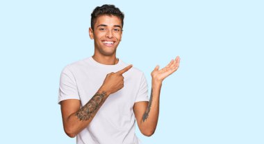 Genç, yakışıklı, Afro-Amerikalı, günlük beyaz tişört giyen, hayrete düşmüş ve kameraya gülümseyen bir adam.. 