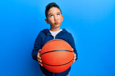 Küçük İspanyol çocuk basketbol topu tutuyor, ağzıyla balık suratı yapıyor, gözlerini kıstı, deli ve komik.. 