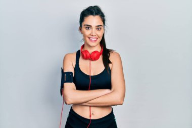 Spor kıyafetleri giyen ve kulaklık takan, kollarını kavuşturup kameraya gülümseyen İspanyol bir kız. pozitif kişi. 