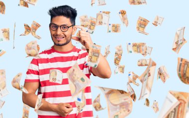 Yakışıklı Latin Amerikalı genç adam günlük kıyafetler ve gözlük takıyor gülümsüyor ve el hareketleriyle küçük boy işaretler yapıyor ve kameraya bakıyor. ölçüm kavramı.