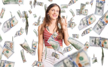 Güzel, beyaz, günlük kıyafetler giyen genç bir kadın üç numaralı parmaklarıyla gülümseyerek kendinden emin ve mutlu bir şekilde onu işaret ediyor..