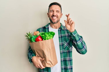 Sakallı yakışıklı bir adam, elinde torba, elinde alışveriş poşeti var. Umut dolu ve gözleri kapalı bir şekilde gülümsüyor. Şans ve batıl inançlar. 